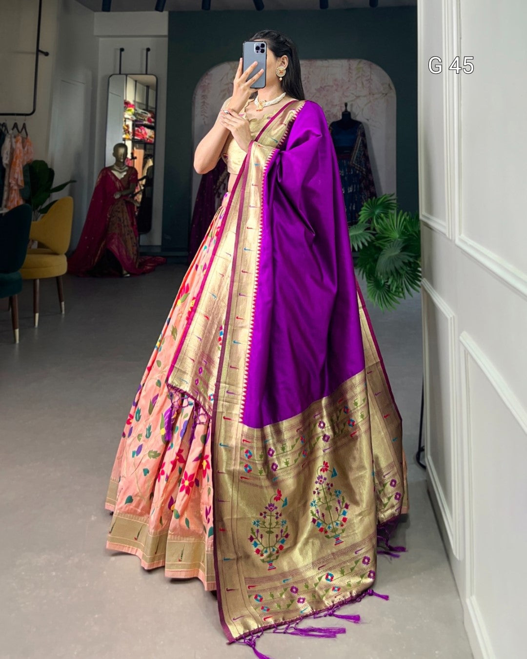 Woman wearing a traditional saree with a purple blouse and pink and gold border in a room.