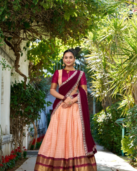 Woman in a maroon and peach saree standing in a garden