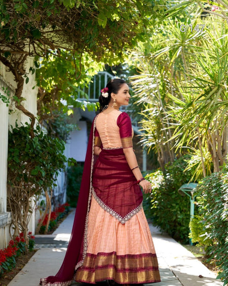 Woman in a traditional maroon and beige saree walking through a garden.