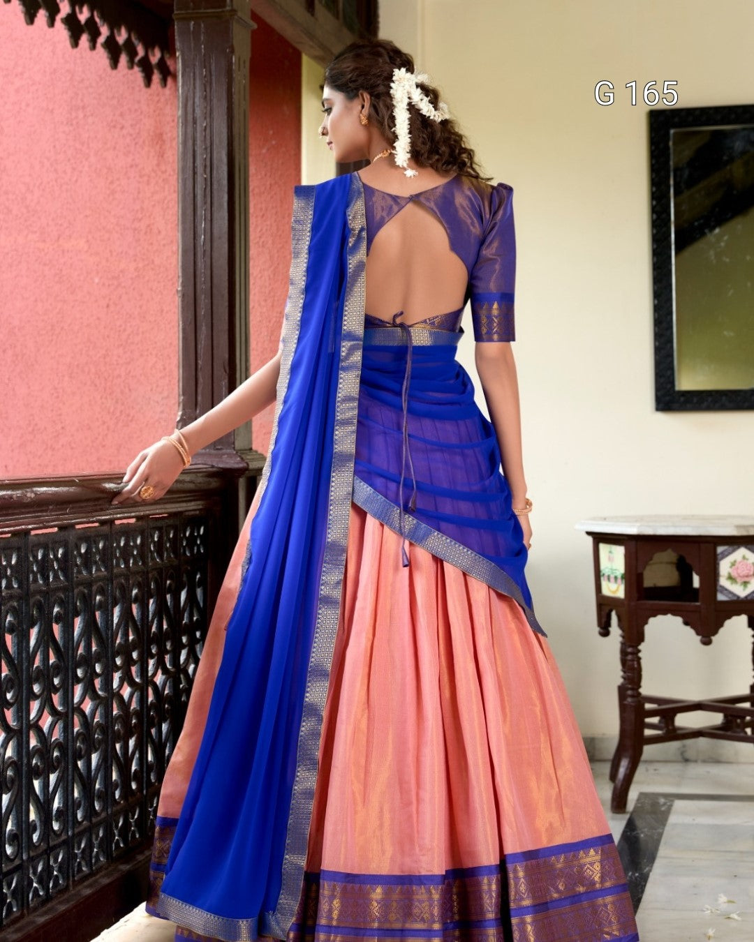 Woman wearing a traditional saree with a blue blouse and pink skirt in an indoor setting.