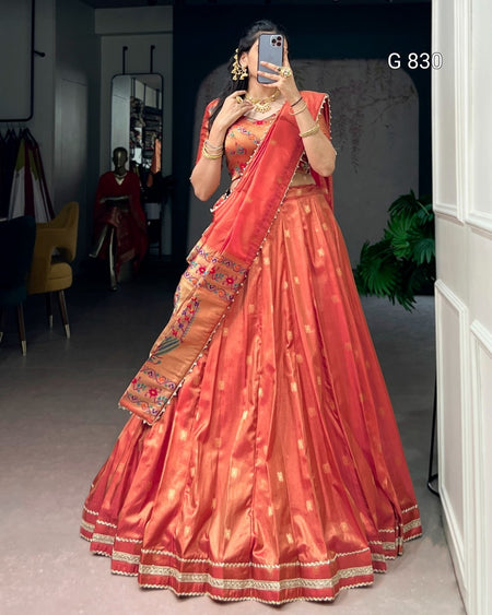 Person wearing a traditional orange saree with gold details indoors.