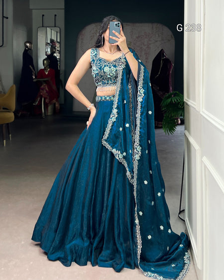 Woman in a blue traditional outfit with intricate designs, standing indoors.