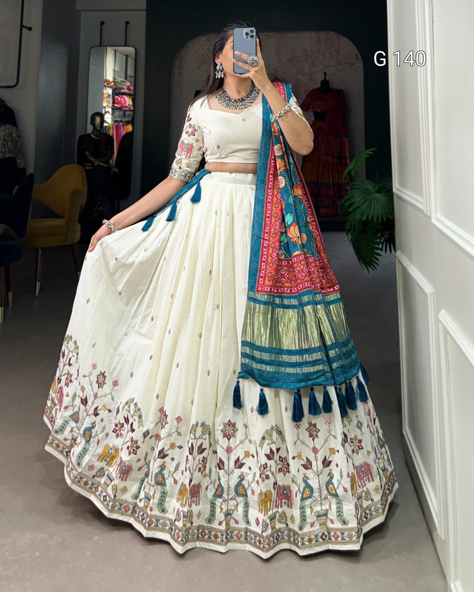 Woman in a traditional white and blue embroidered outfit with colorful dupatta in a room.