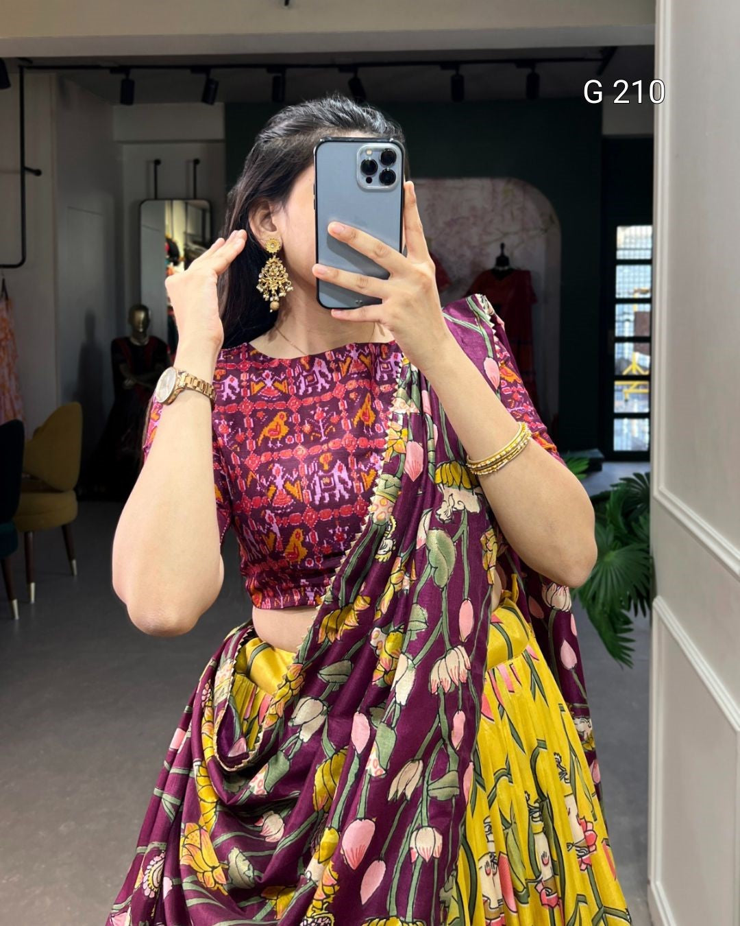 Person wearing a colorful traditional outfit with a patterned top and yellow skirt, taking a mirror selfie.