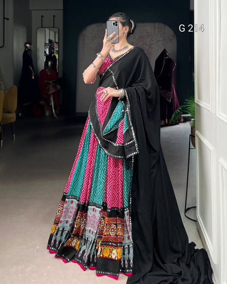 Person wearing a colorful traditional outfit with a black dupatta in an indoor setting.