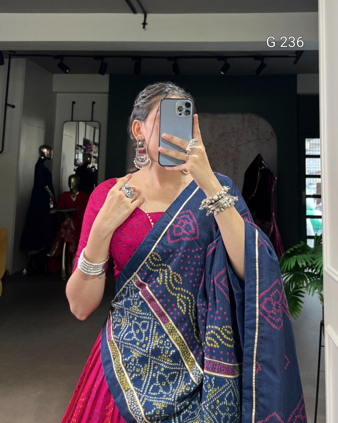 Person wearing a blue and pink saree with jewelry, taking a mirror selfie.