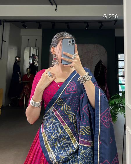 Person wearing a blue and pink saree with jewelry, taking a mirror selfie.