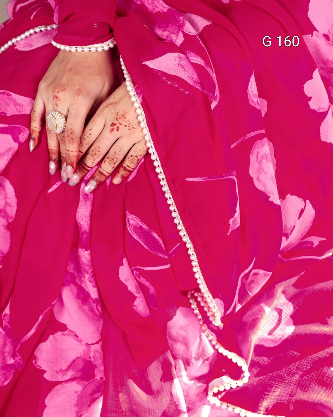 Close-up of a pink fabric with floral patterns and a hand wearing a ring.