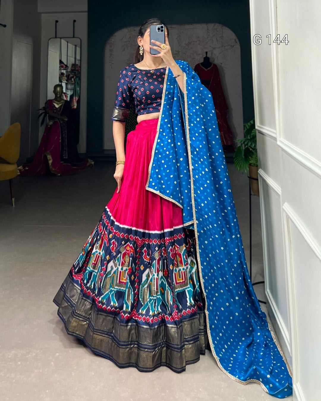 Person wearing a traditional outfit with a blue dupatta and colorful skirt in a room.