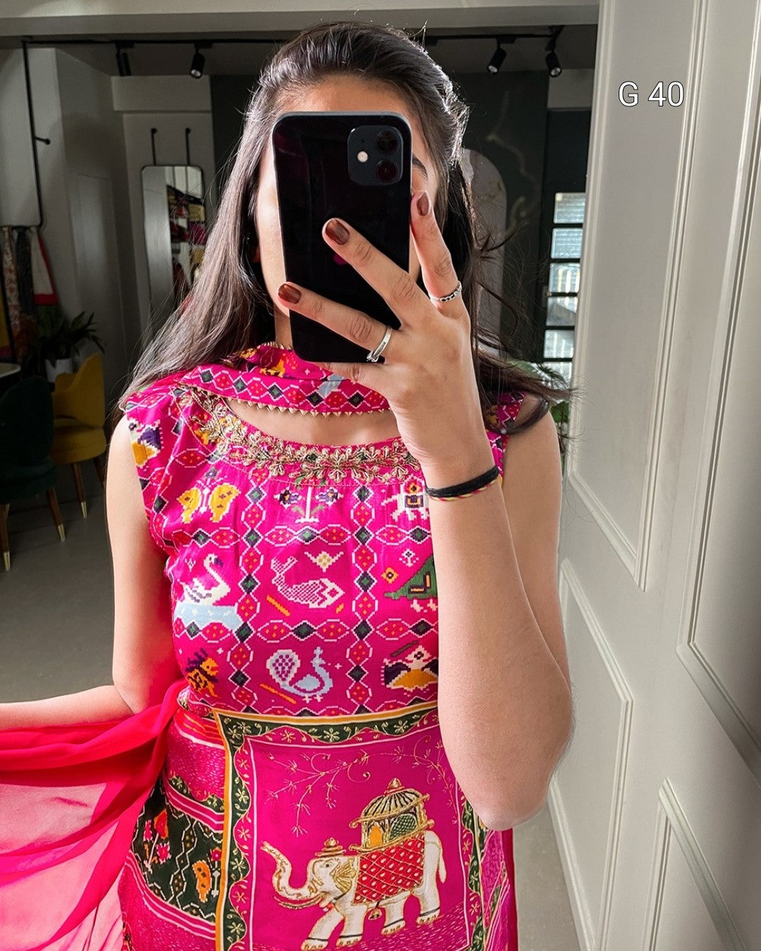 Person wearing a vibrant pink traditional outfit with intricate patterns, taking a mirror selfie.