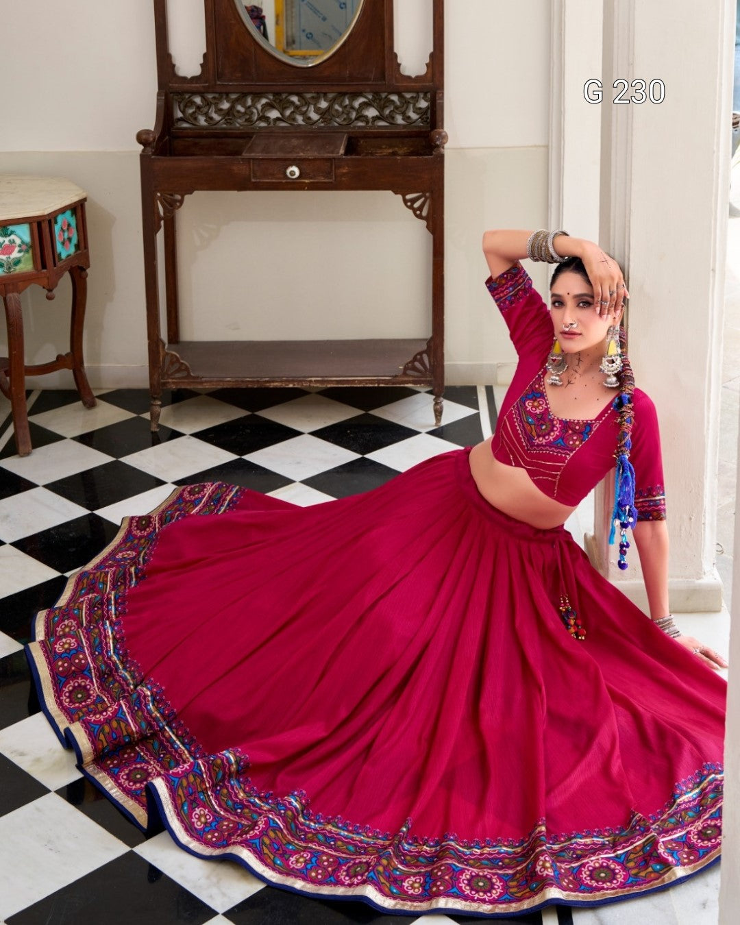 Woman in a vibrant red saree with intricate patterns in a room with checkered floor and wooden furniture.