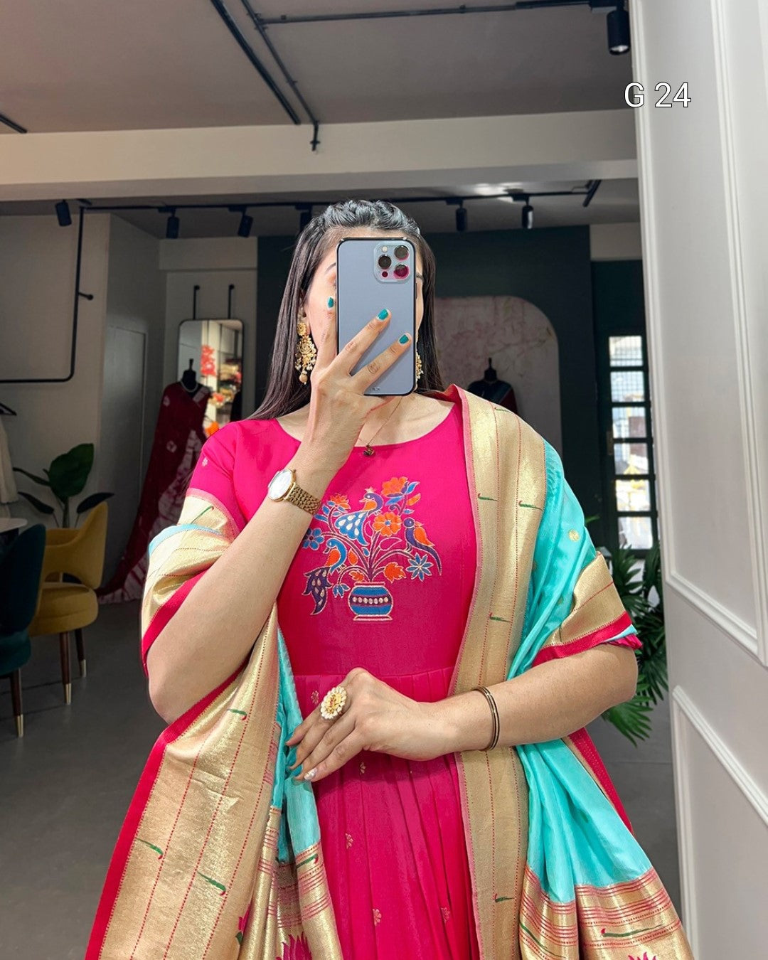 Woman taking a mirror selfie wearing a pink dress with floral patterns and a beige and blue dupatta.