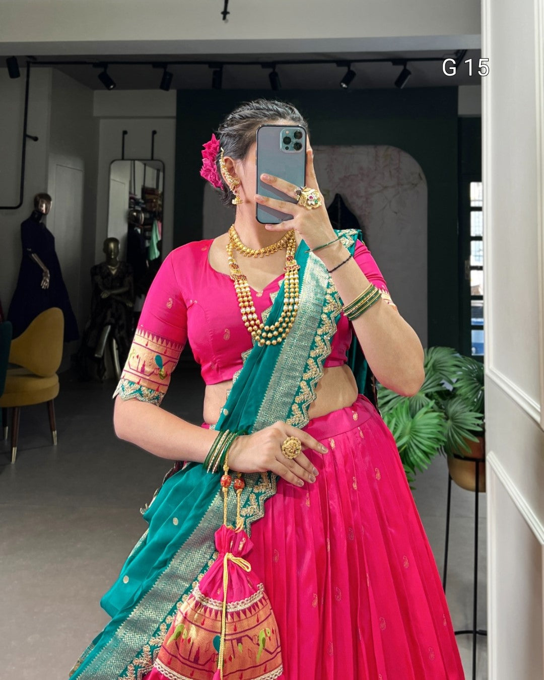 Person wearing a bright pink traditional outfit with a teal saree in a room.
