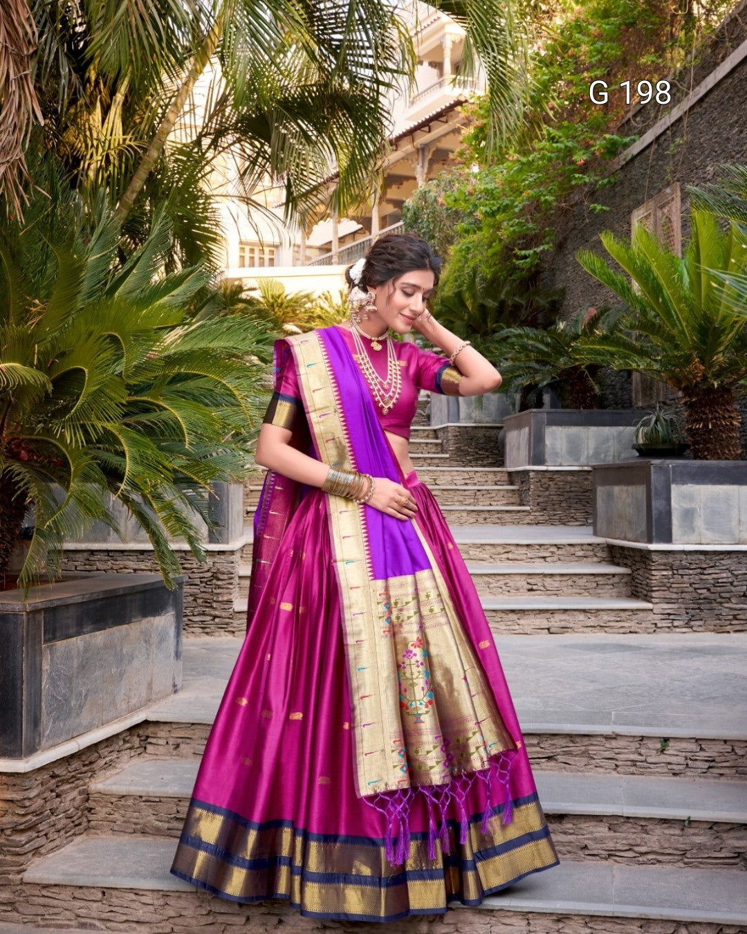 Woman in a vibrant purple and pink saree with gold border standing outdoors.