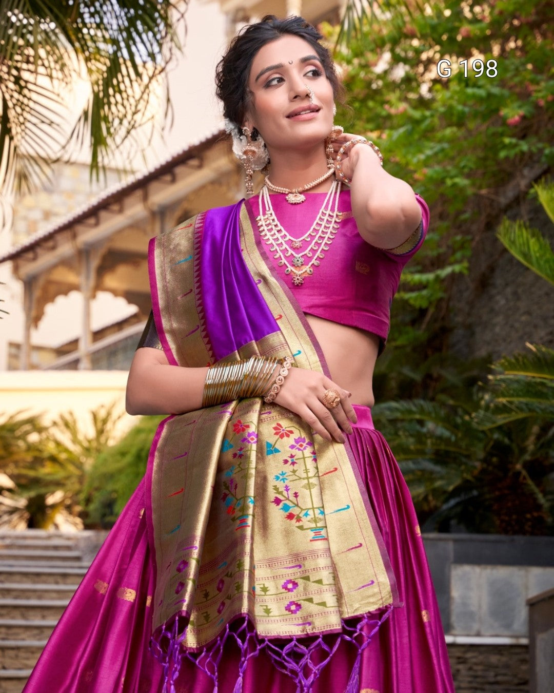 Woman in a traditional pink and gold saree with jewelry outdoors.