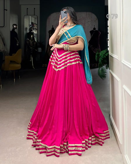 Person wearing a bright pink saree with a blue blouse in a room.