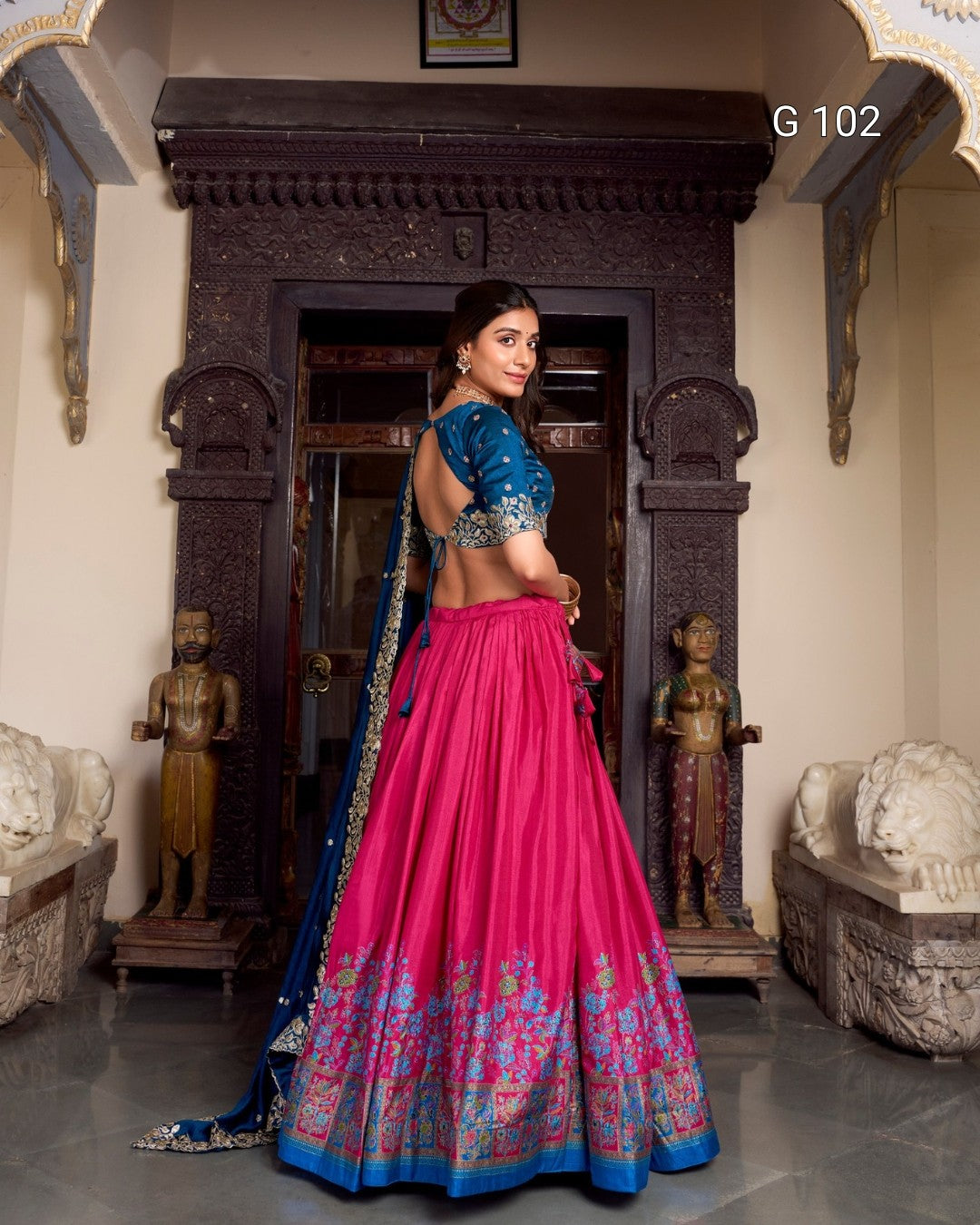Woman in a traditional pink and blue outfit standing in an ornate room.