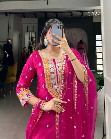 Woman taking a mirror selfie wearing a vibrant pink traditional outfit with intricate designs.