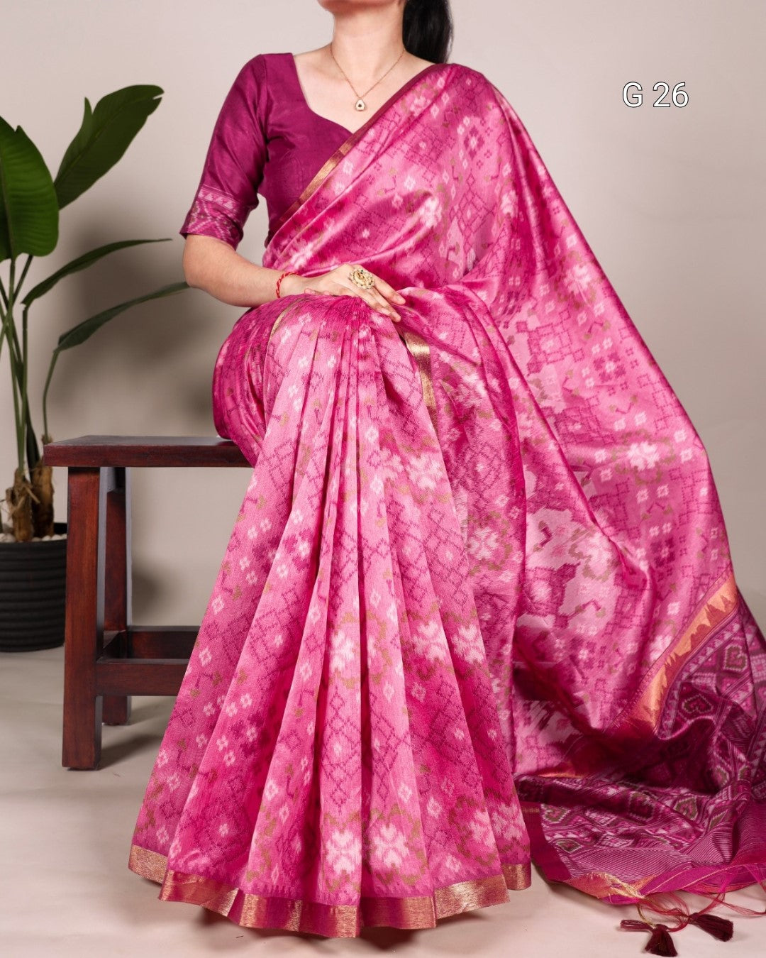 Woman wearing a pink saree with a subtle pattern, sitting on a chair.