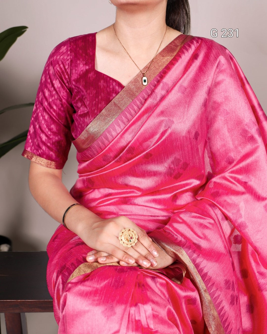 Person wearing a pink saree with a brown border, holding a decorative ring.