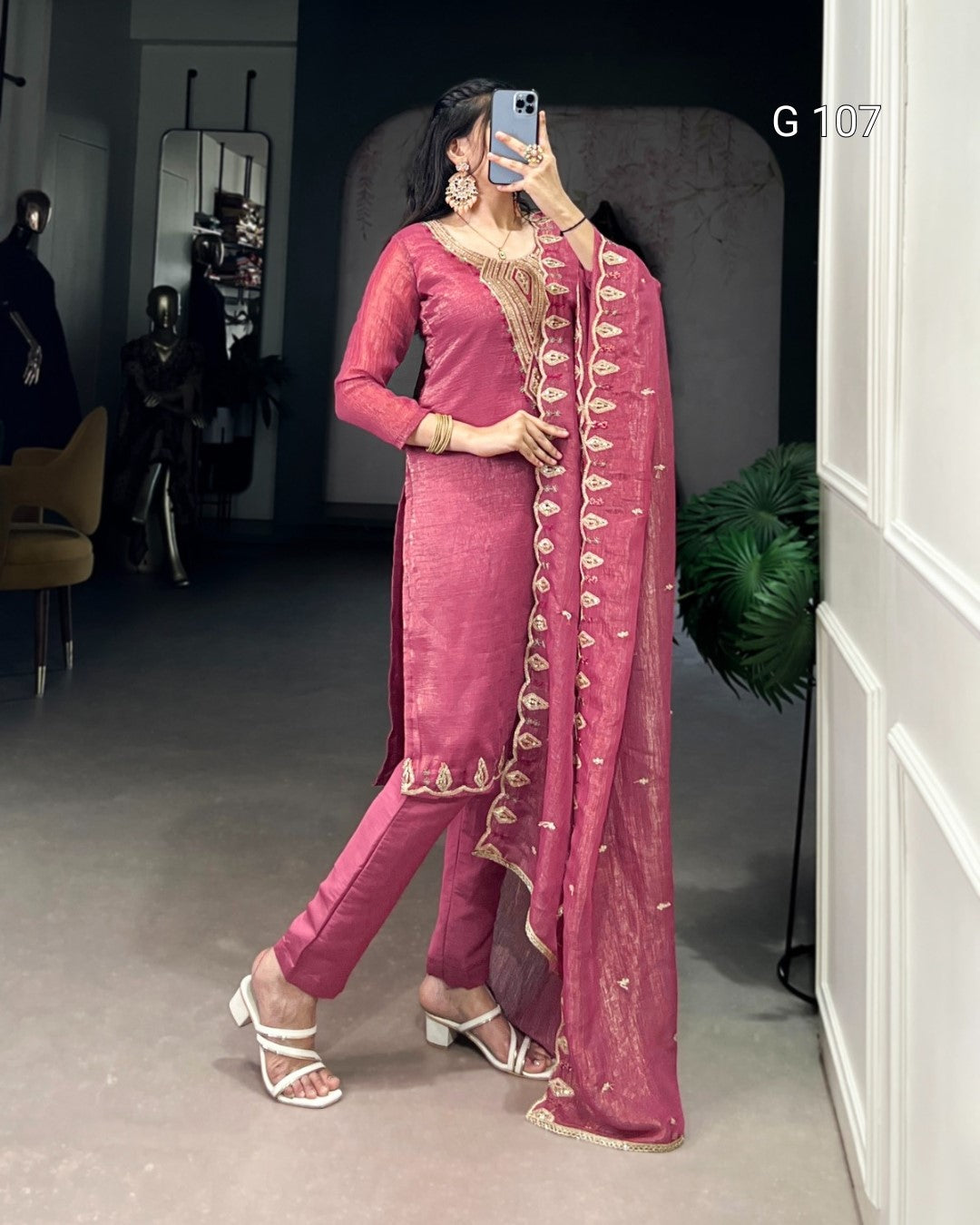Woman in a pink traditional outfit with gold embroidery taking a mirror selfie.
