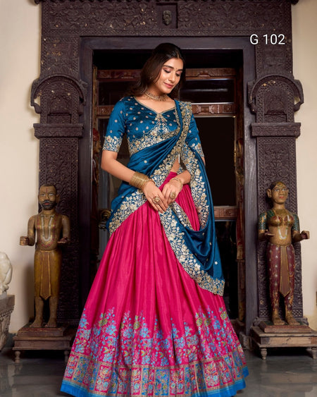 Woman in a blue and pink saree standing in front of a decorative entrance.