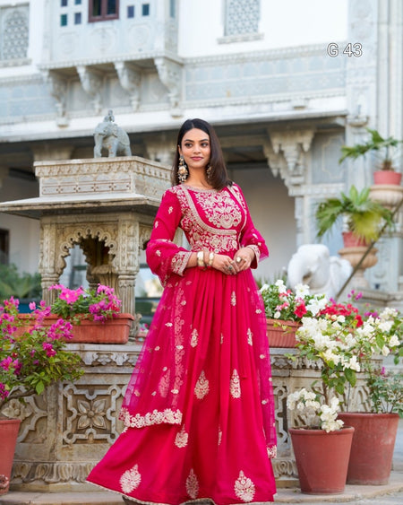 Woman in a red traditional outfit standing in front of an architectural structure with flowers.