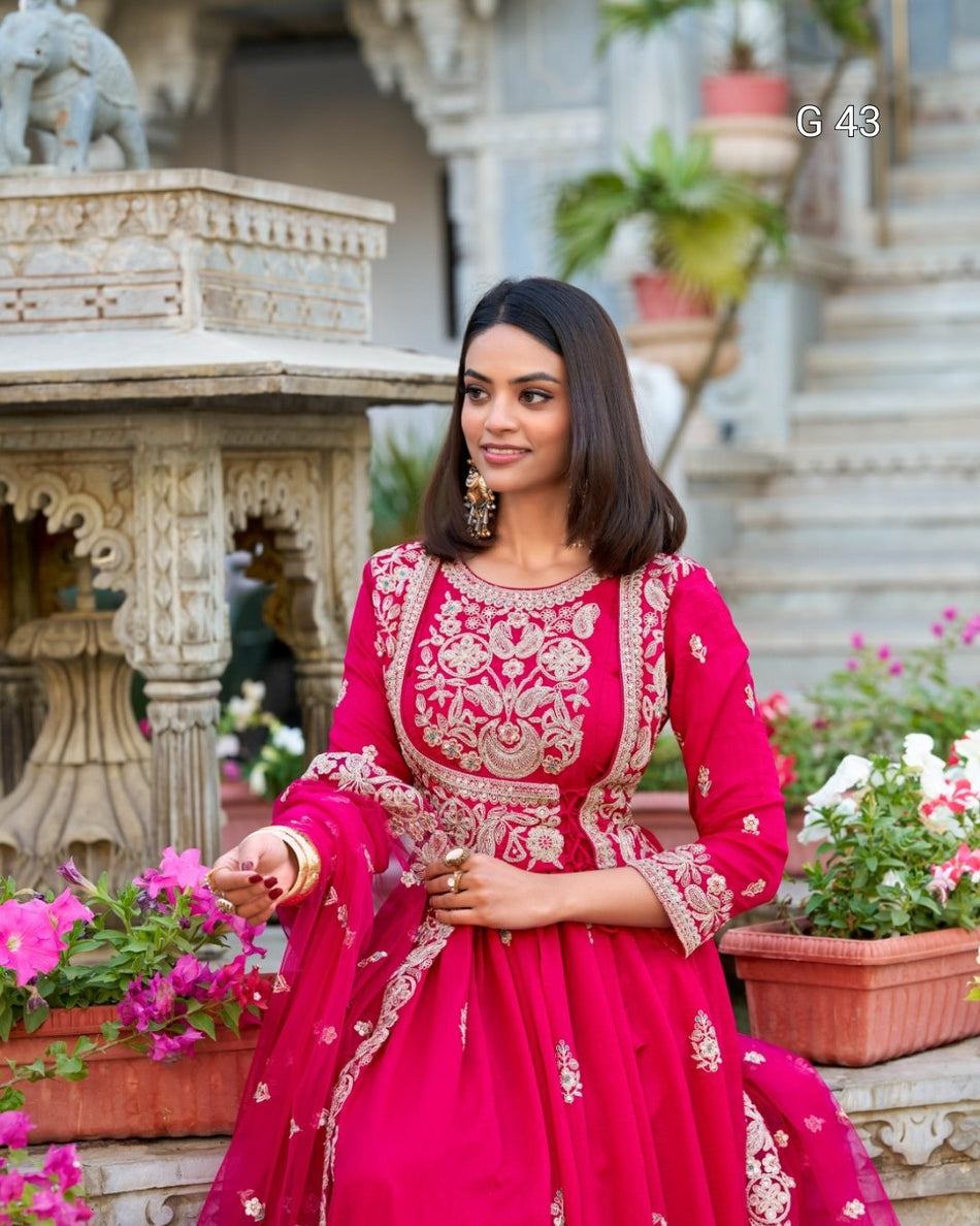 Woman in a pink traditional outfit standing outdoors with decorative elements in the background