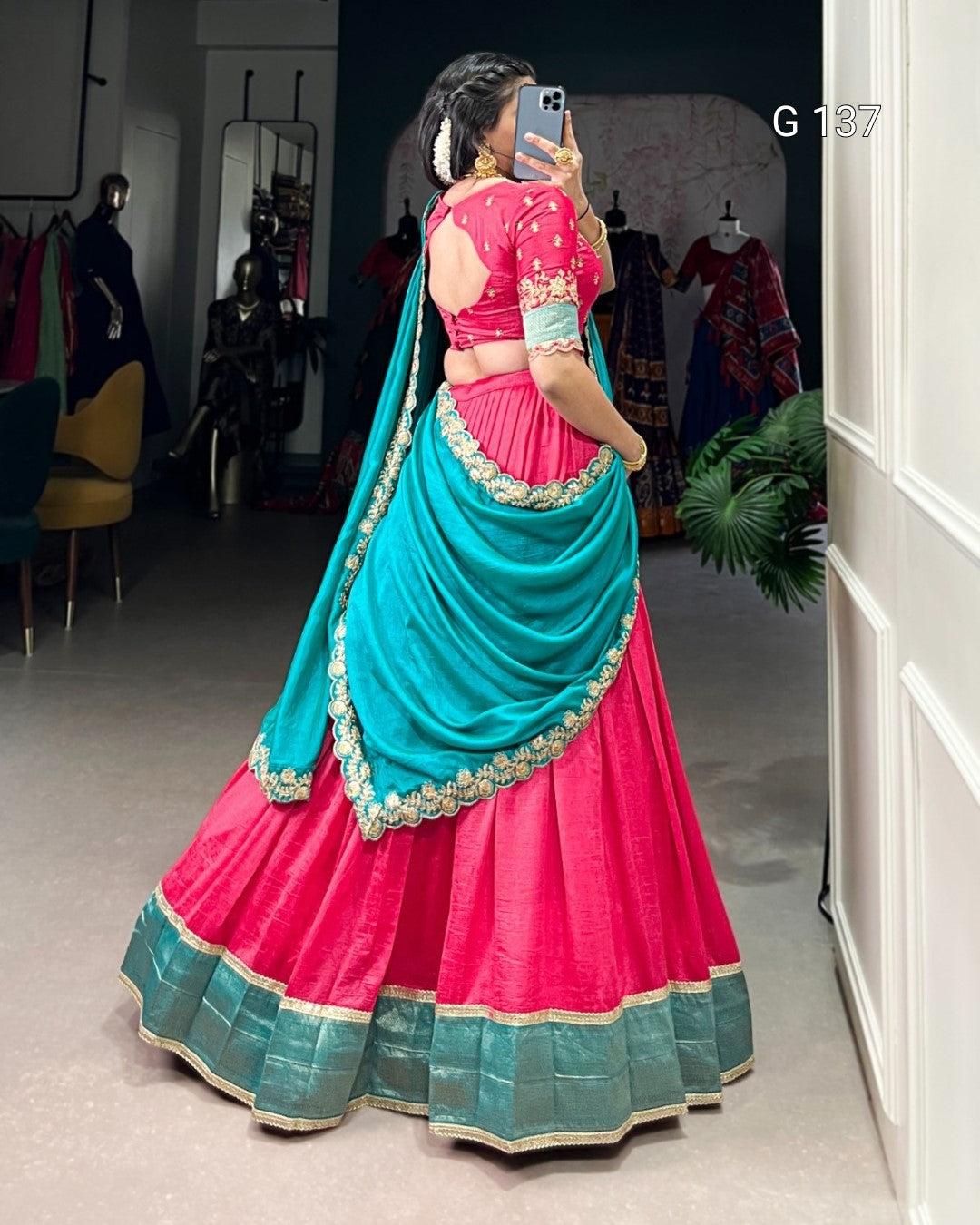 Person wearing a pink and teal traditional outfit in a room with mirrors and clothing racks.