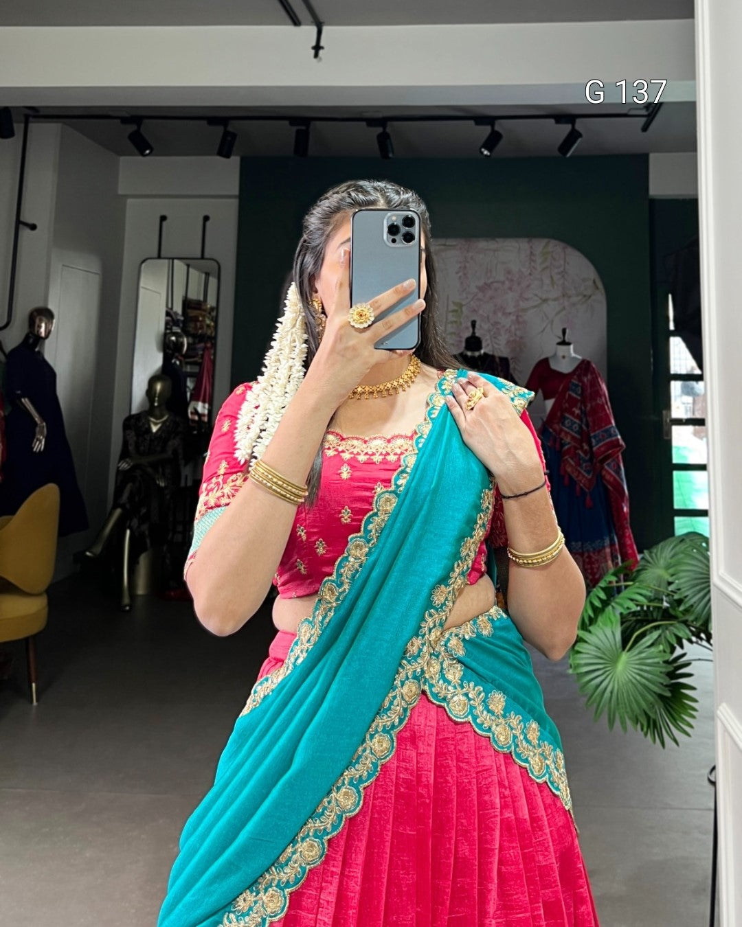 Woman taking a mirror selfie wearing a pink and blue saree with gold accents.