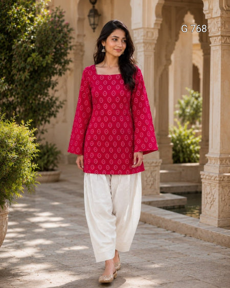 Woman wearing a red patterned top and white pants walking in an outdoor setting with architectural elements.