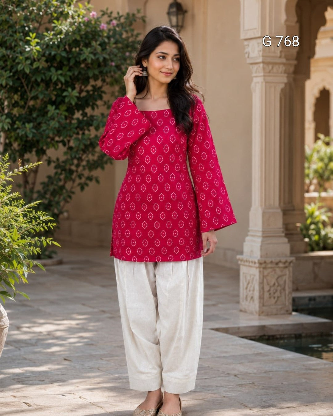 Woman wearing a pink patterned top and white pants standing in an outdoor setting.