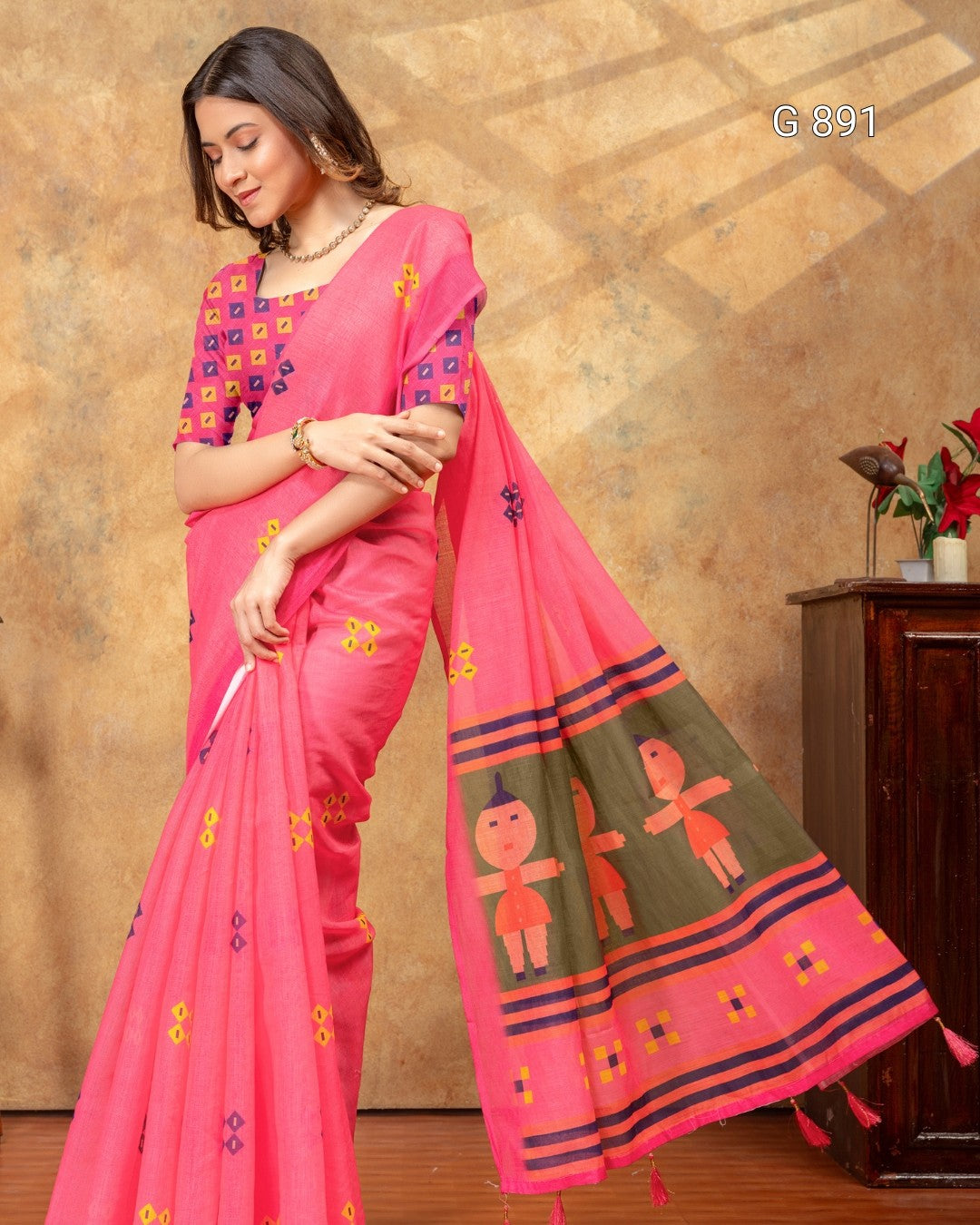 Woman wearing a pink saree with intricate designs against a warm-toned wall.