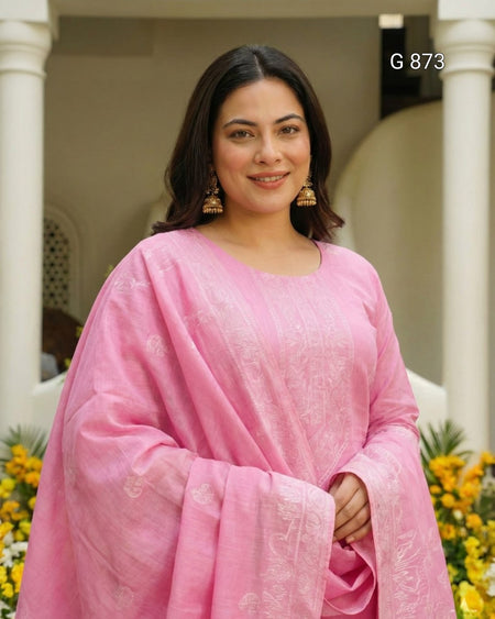 Woman in a pink saree standing in front of a decorative background with columns and flowers.