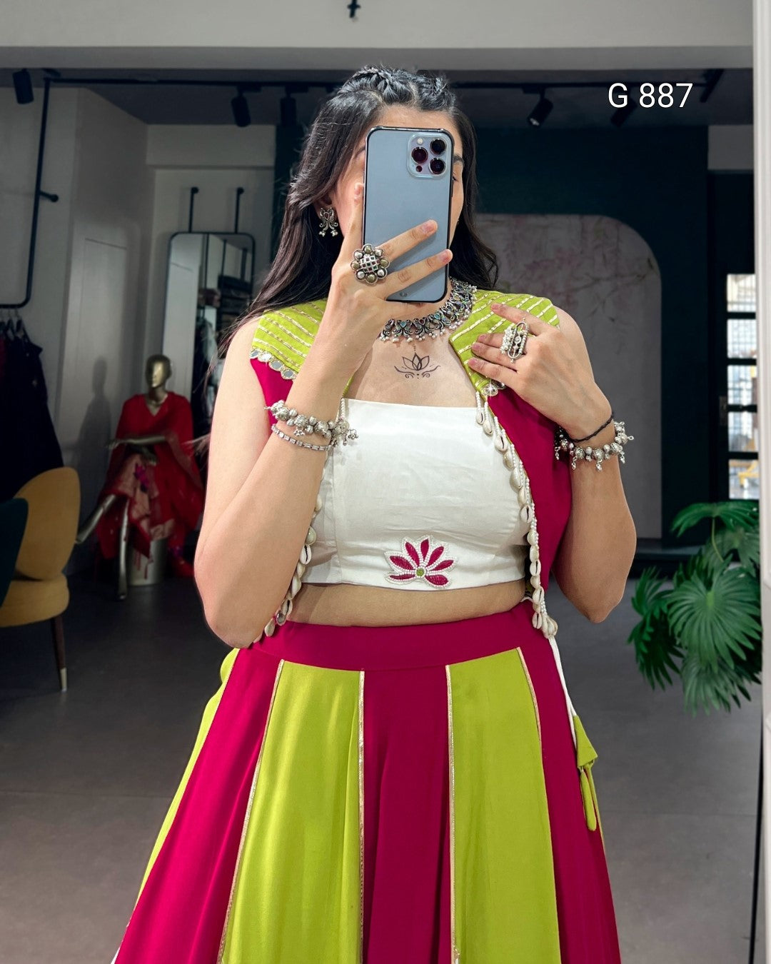 Person wearing a colorful traditional outfit with a white top and pink and green skirt, taking a mirror selfie.