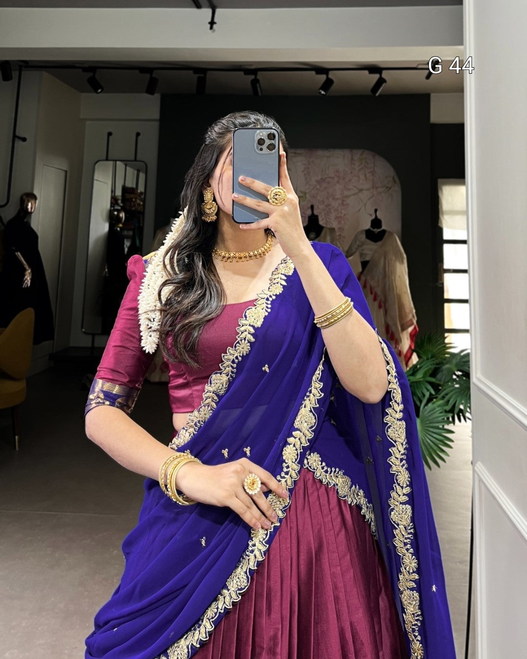 Woman wearing a purple and blue saree with gold jewelry in a room.