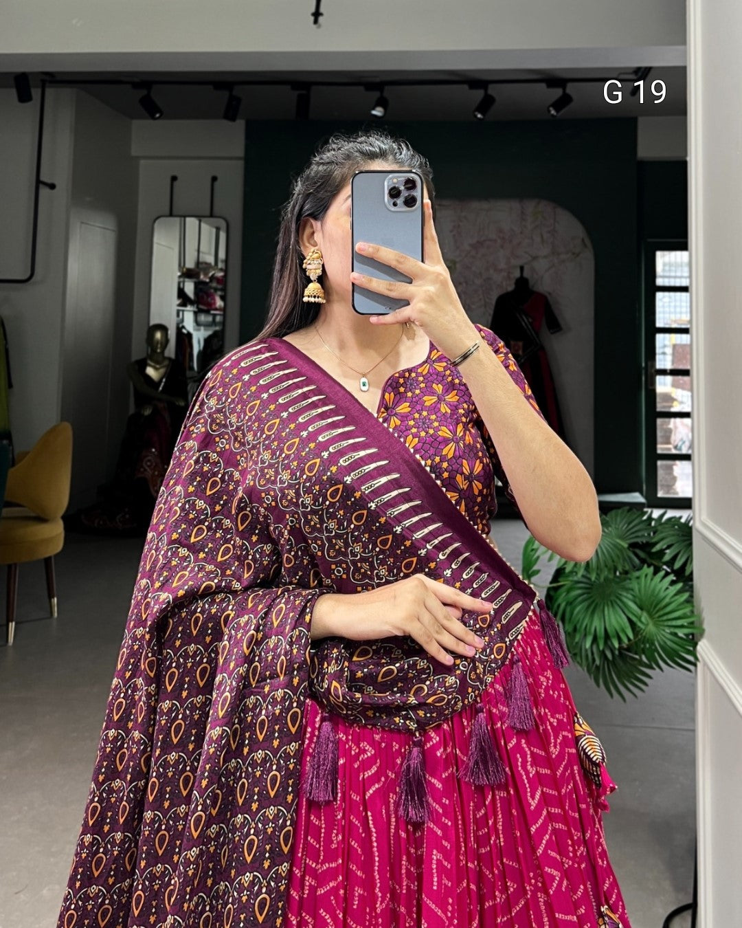 Woman taking a mirror selfie wearing a pink and purple patterned saree.
