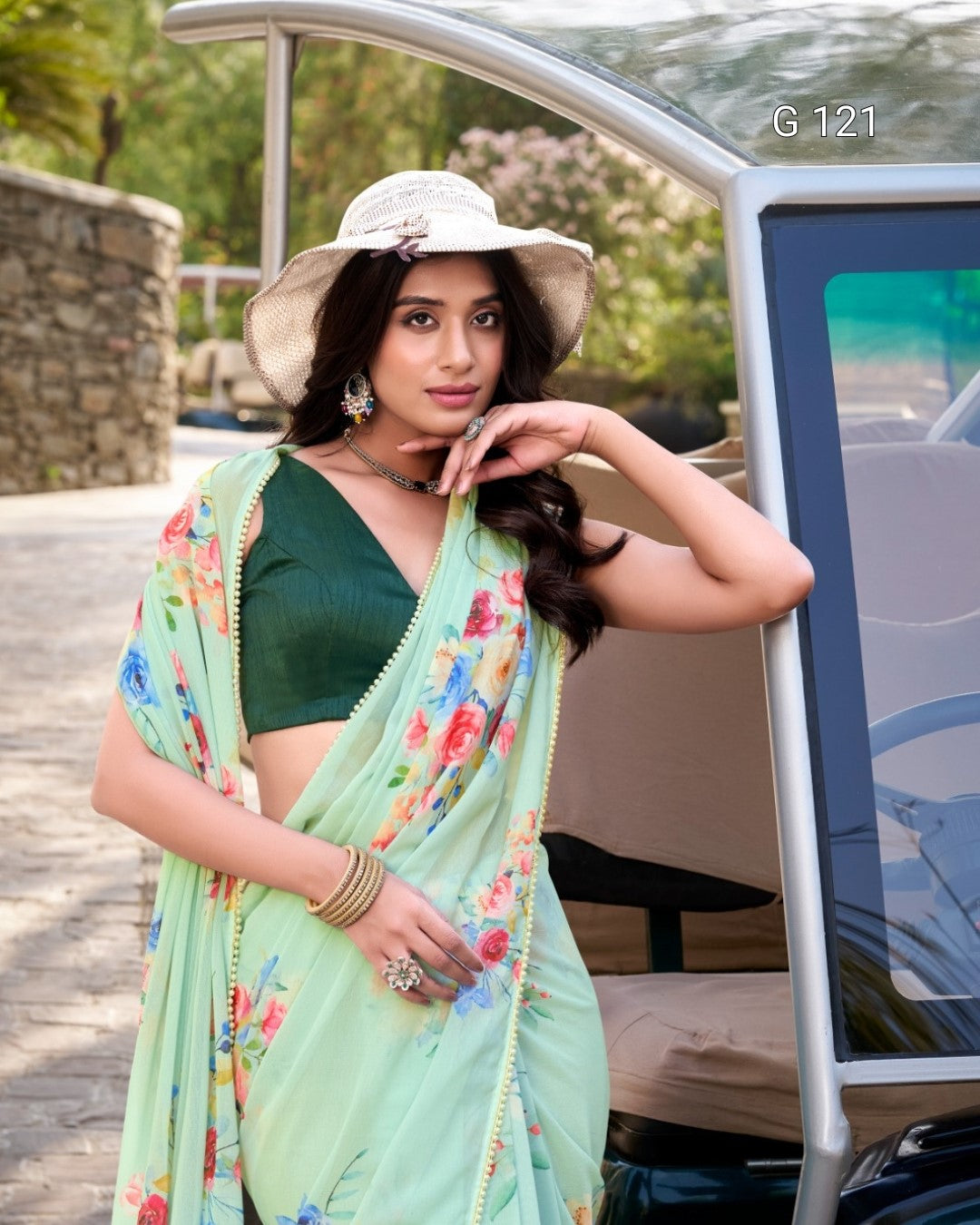 Woman in a green saree with floral patterns standing next to a car