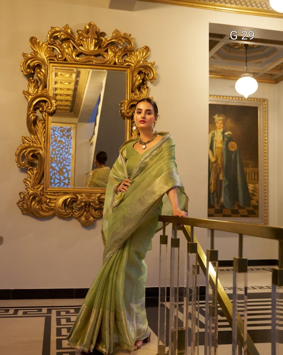 Woman in a green saree standing in front of an ornate mirror in an elegant interior setting.