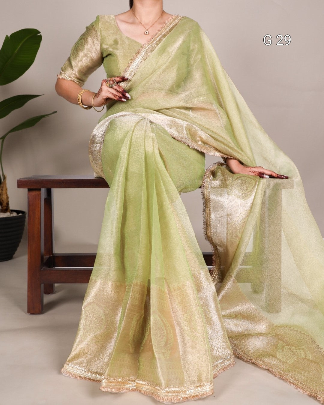 Woman wearing a light green saree with gold border, sitting on a chair.