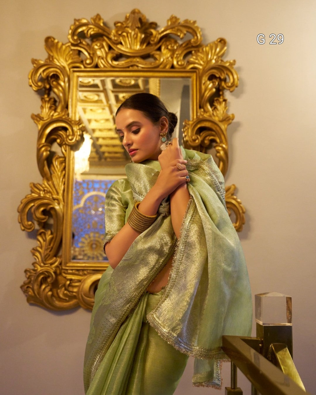 Woman holding a light green saree in front of an ornate gold mirror.