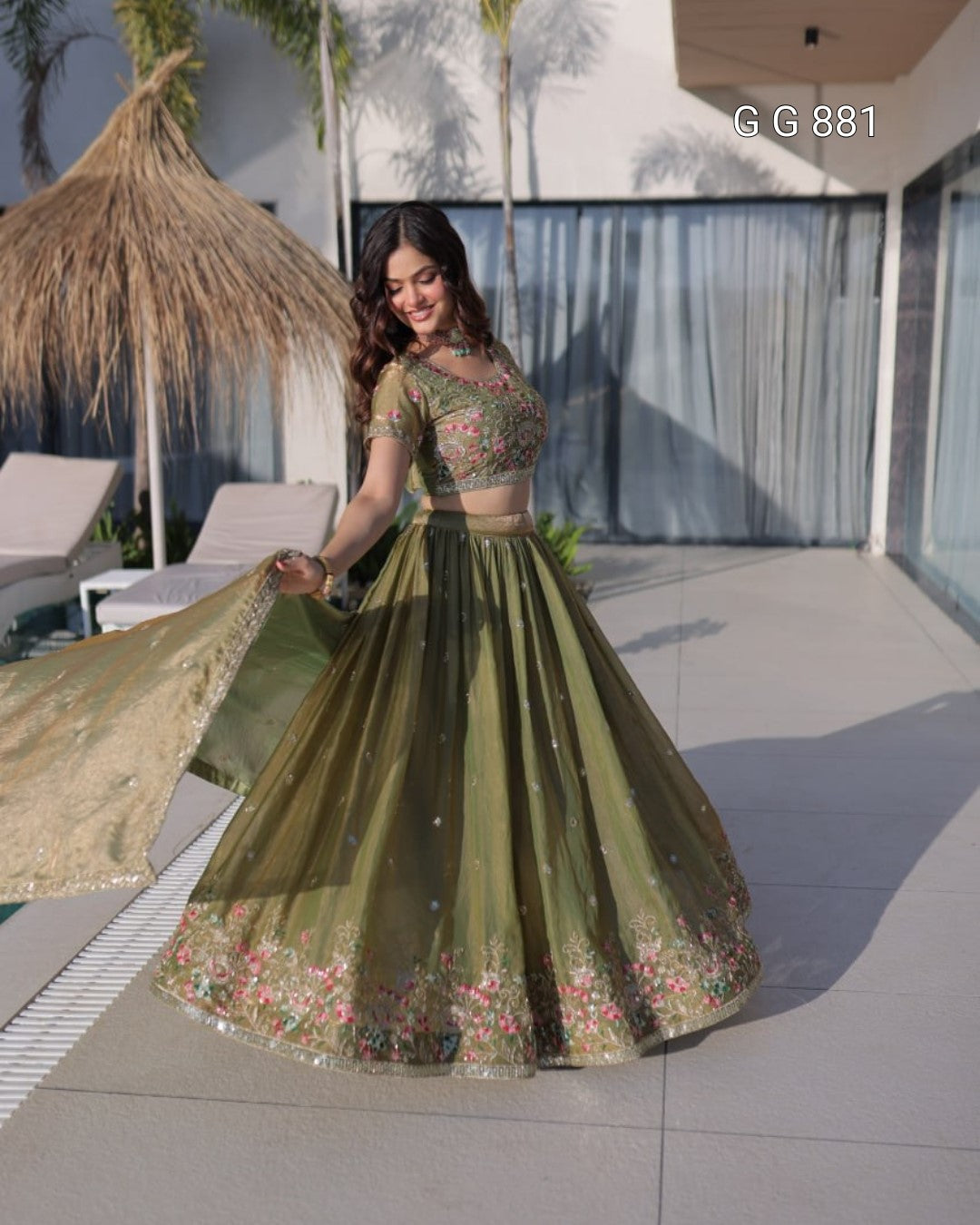 Woman in a green embroidered traditional outfit standing outdoors with modern architecture in the background.