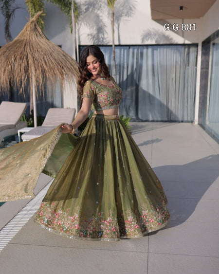 Woman in a green embroidered traditional outfit standing outdoors with modern architecture in the background.