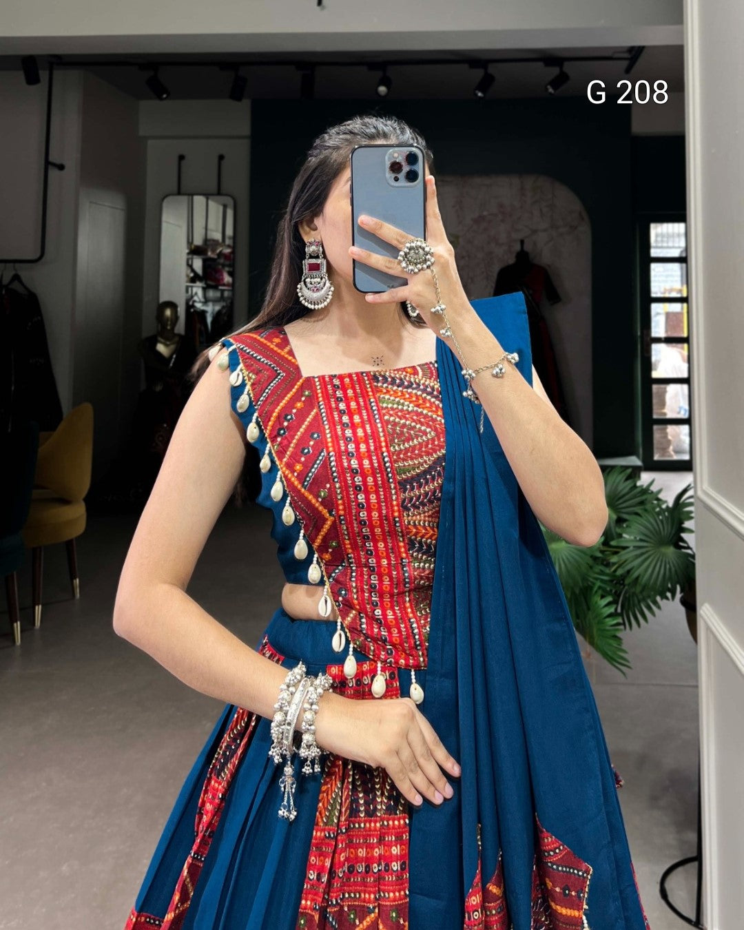 Person wearing a colorful traditional outfit with a blue dupatta, taking a mirror selfie.