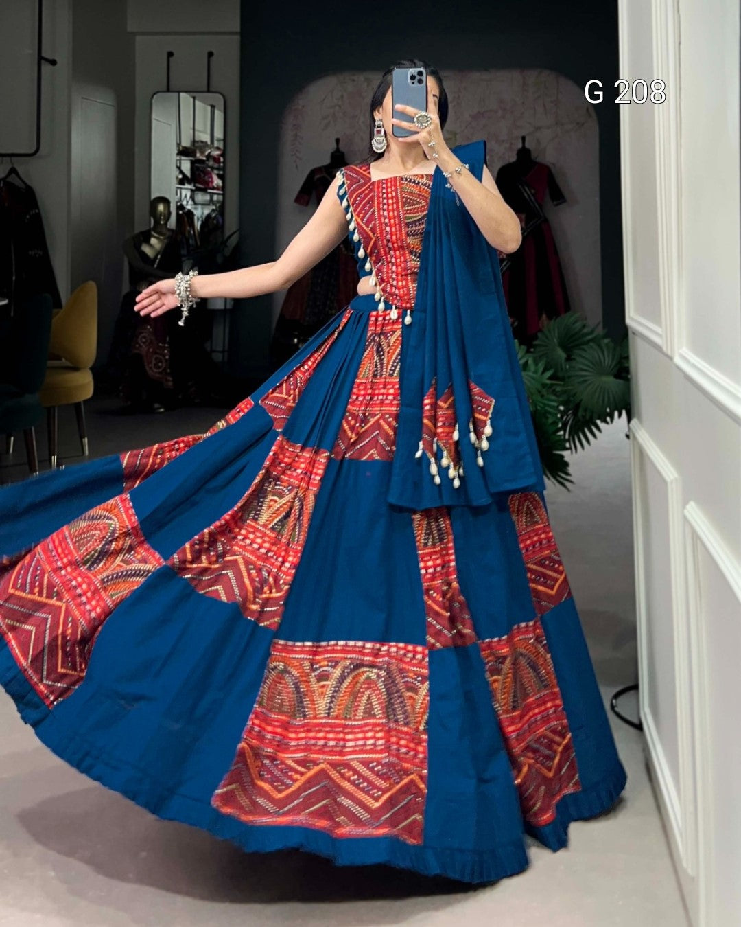 Woman in a blue and red patterned saree taking a mirror selfie.