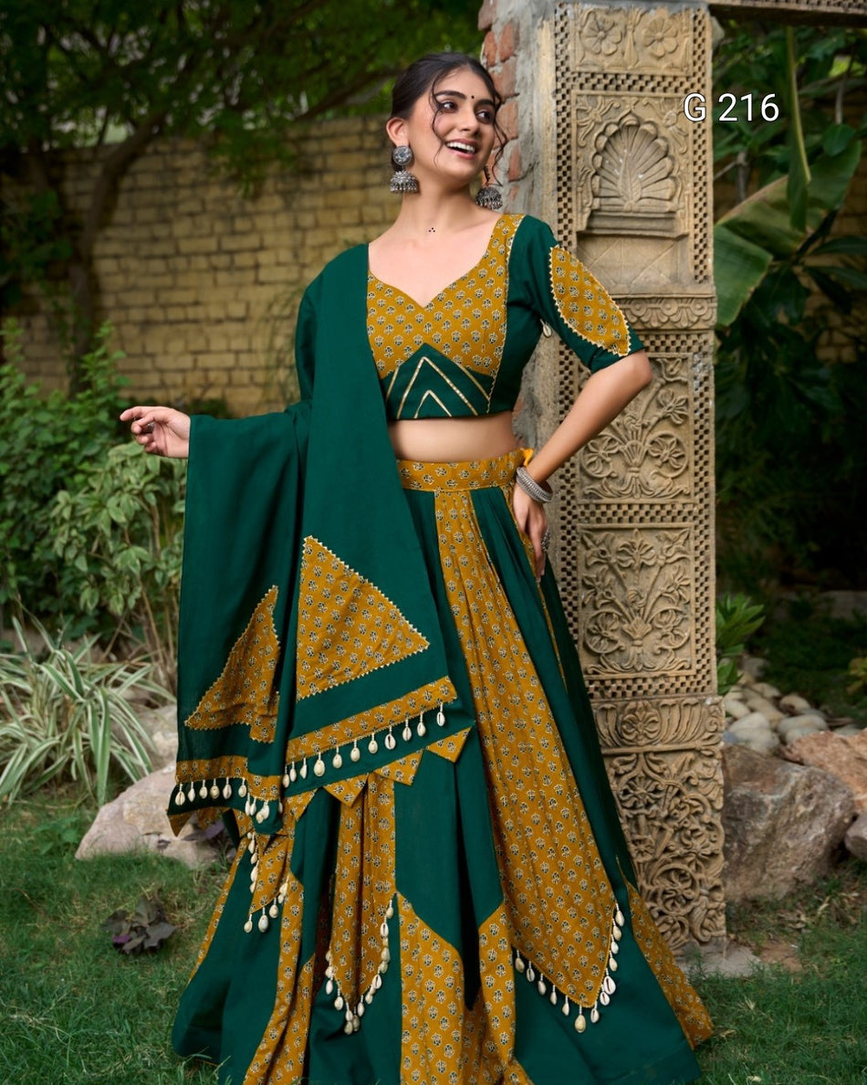 Woman in a green and gold traditional outfit standing outdoors near decorative stone architecture.