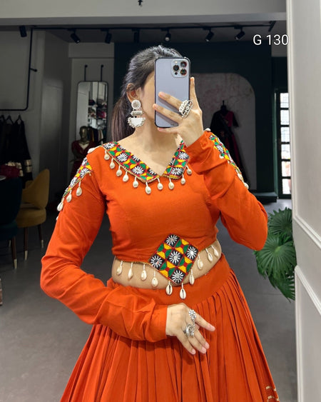 Person wearing an orange traditional outfit with jewelry indoors.