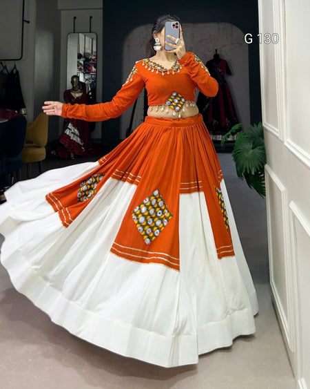 Person wearing an orange and white traditional outfit with intricate designs, standing in a room.