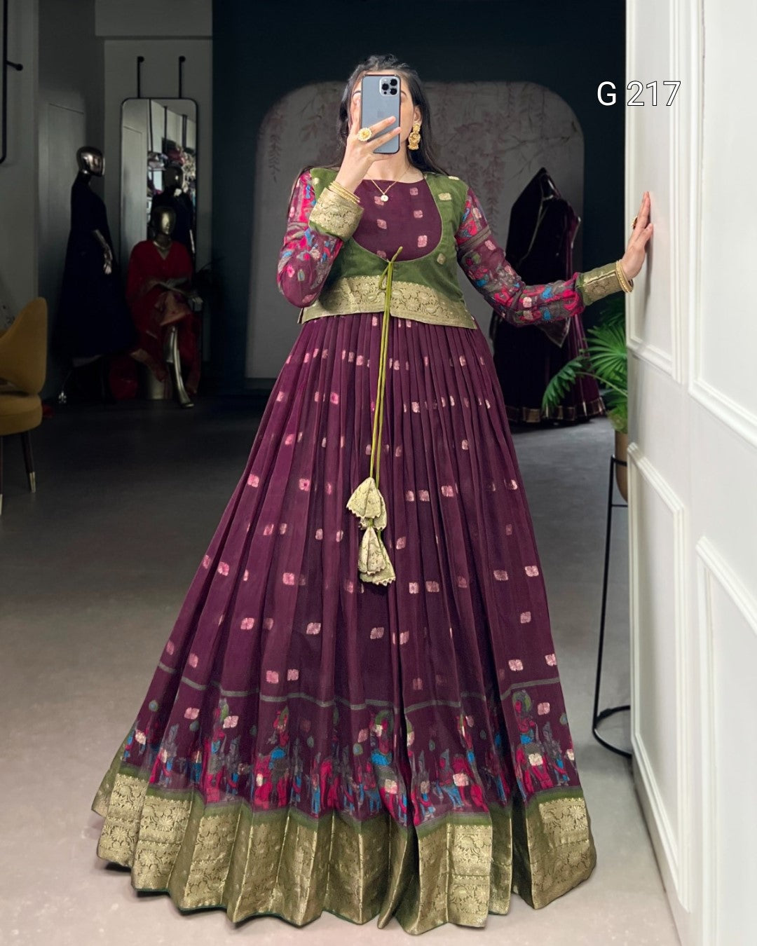 Person wearing a traditional outfit with a long purple dress and green top, standing in a room.