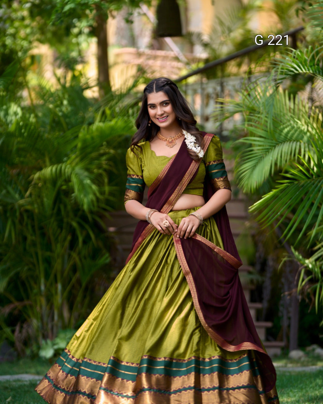 Woman in a green and maroon traditional outfit standing in a garden.